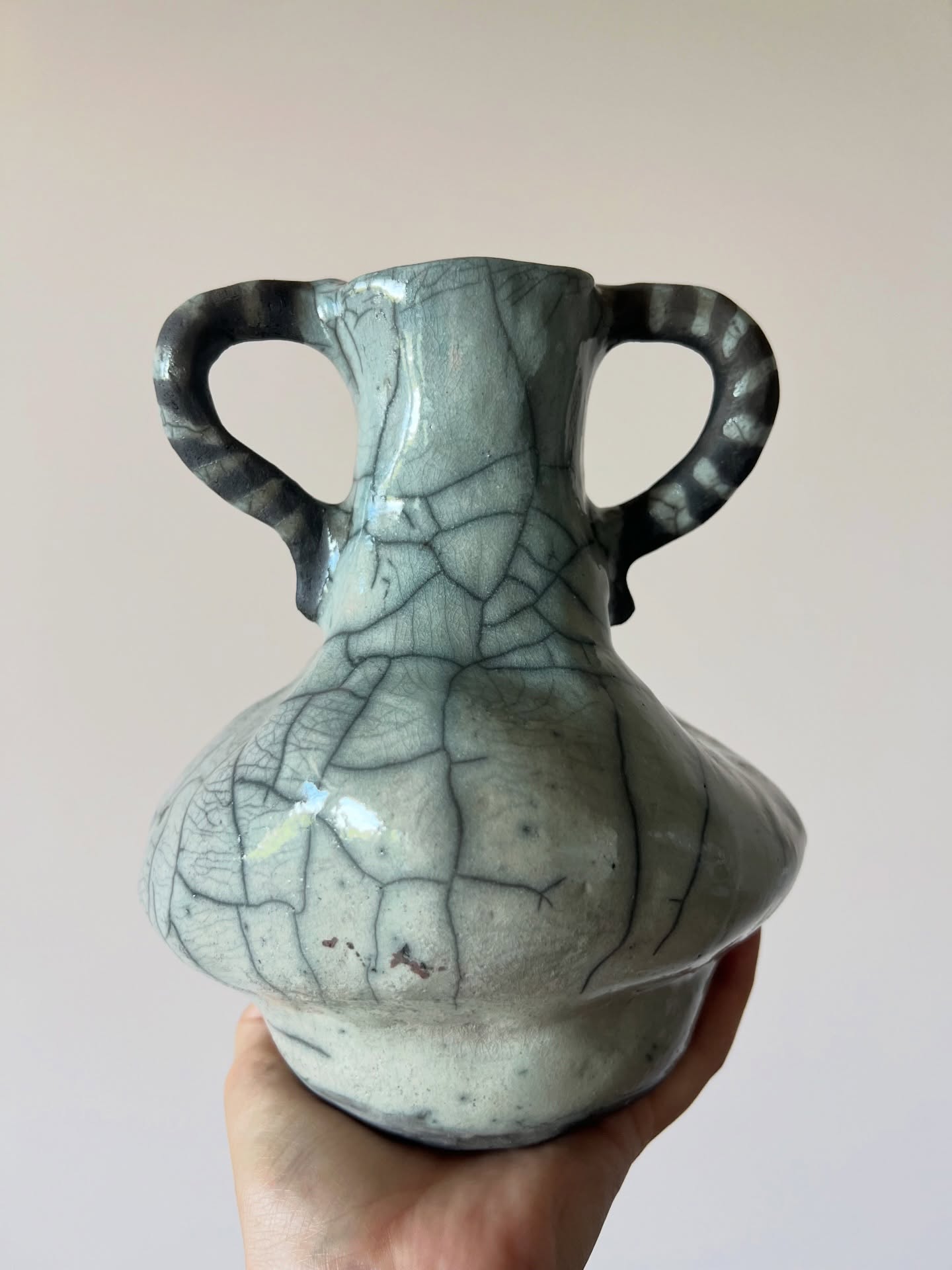 A hand holding a two-handled glazed Potpuri ceramic vase